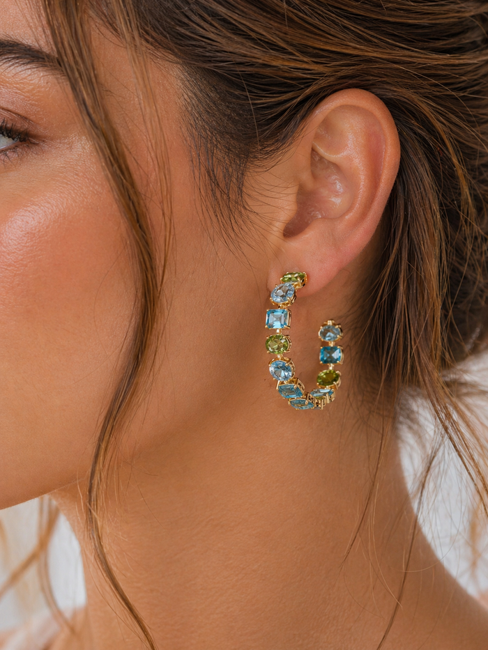 Blue and green jeweled hoop earrings from Private Label featuring sparkling stones and gold-tone hoops.