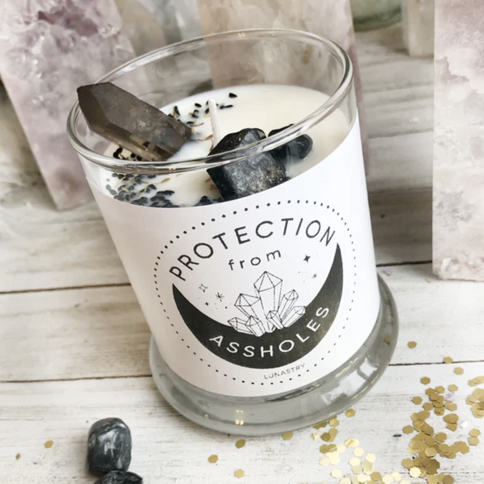 Lunastry Protection from Assholes Candle with a humorous label, featuring a tall white candle in a glass holder.